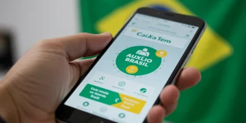 Tela do aplicativo Caixa Tem com saldo do Auxílio Brasil e opções de movimentação, sendo segurada por uma pessoa.