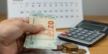 Mão segurando notas de reais com calculadora e calendário 2026 ao fundo, simbolizando o novo cálculo do FGTS.